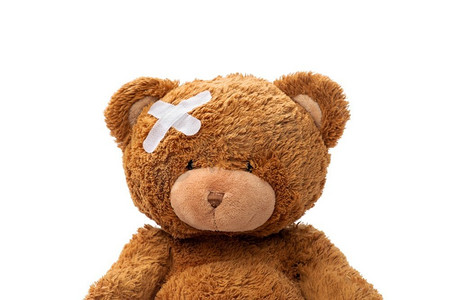 医药，保健和儿童概念—泰迪熊玩具有医疗补丁在头上在白色背景。头部带医用贴片玩具熊