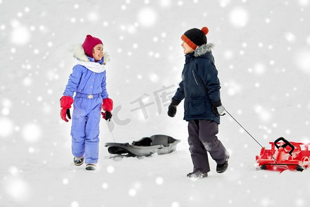 冬天小朋友摄影照片_童年、雪橇和季节概念-冬天带着雪橇的快乐小朋友。冬天玩雪橇的快乐小朋友