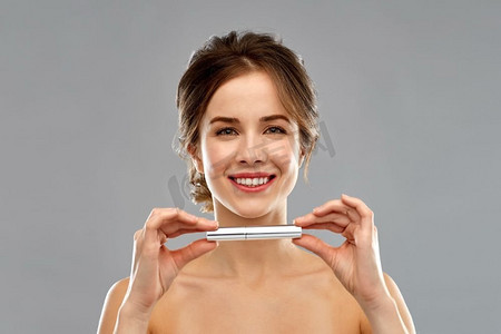 美丽，弥补和化妆品概念—微笑的年轻妇女拿着睫毛膏在灰色背景女士拿着睫毛膏管