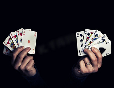 红色的的心摄影照片_白人男性手握两个皇家同花顺扑克组合的心和黑桃。低调的灯光组成，孤立在黑色背景
