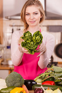 抱着蔬菜摄影照片_快乐的年轻女子，烹饪厨师显示持有绿色生菜。女性爱蔬菜即将烹饪.. Womna抱着绿色生菜