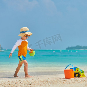家庭度假摄影照片_三岁的蹒跚学步的男孩在海滩上玩沙滩玩具。暑假在马尔代夫度假。