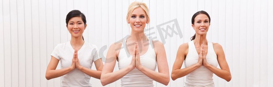 全景网页横幅由三名年轻漂亮女子组成的跨种族团体，在健身房或健身俱乐部练习瑜伽祈祷
