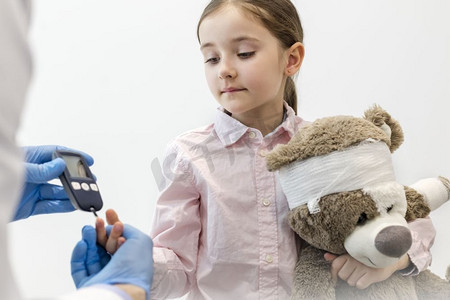 医生在门诊检查糖尿病患者带着泰迪熊的女孩的设备