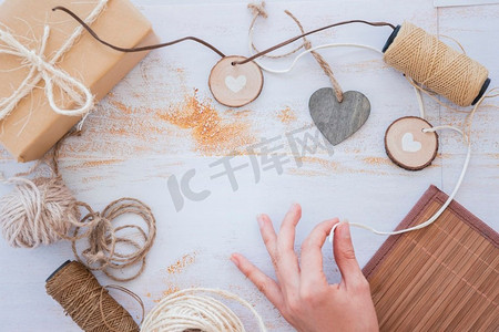 花环摄影照片_关闭手做心脏花环与线轴包装礼品盒白色桌子