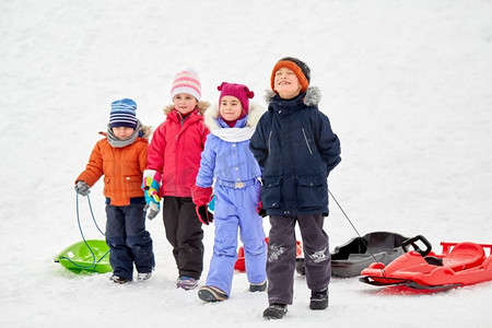 冬天小朋友摄影照片_童年、雪橇和季节概念-一群快乐的小朋友在冬天拉雪橇。冬天玩雪橇的快乐小朋友