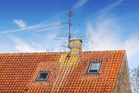 在夏天的蓝天下，屋顶上有天线和烟囱，下面有两扇小窗户