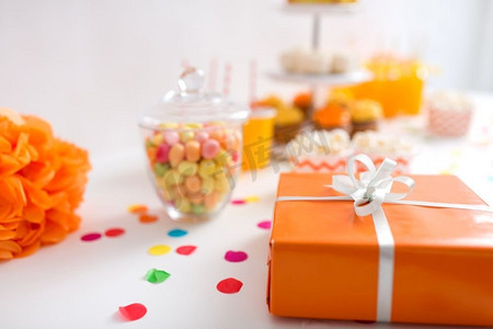 橙色生日摄影照片_派对和节日概念-餐桌上橙色包装的生日礼物的特写。派对桌上放着橙色包装的生日礼物