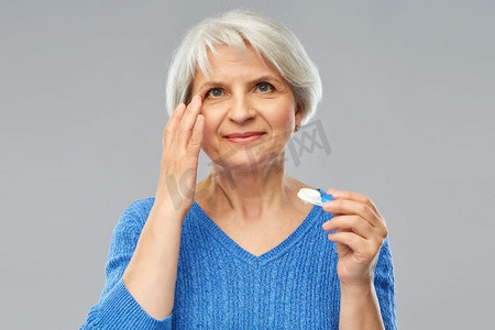 健康，视力和老人观念—年长妇女戴上灰色背景隐形眼镜。戴隐形眼镜的老年女性