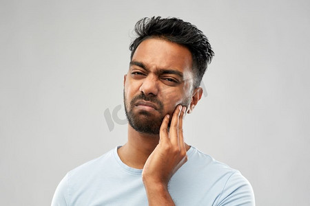 人，牙科和健康问题的概念-印度男子患有牙痛的灰色背景。一名印度男子患牙痛