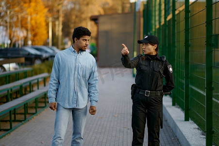 警察妇女向男子显示道路年轻男性路人市民询问方向在街道上。女警察向路人示意