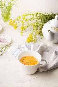 增强免疫摄影照片_在白色桌子上的一杯花草茶与茶壶和新鲜的草药和鲜花。增强免疫力和消化系统。健康的自然疗法