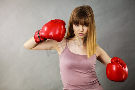 穿着红色拳击手套的运动女，正在打架。工作室拍摄灰色，背景。戴拳击手套的女人