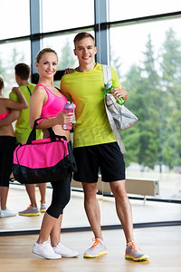 运动、健身、生活方式和人的概念--在健身房带着水瓶和水袋微笑的情侣。健身房里拿着水瓶和水袋的运动情侣