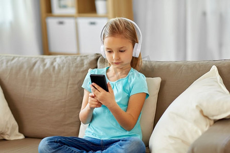 儿童歌曲大赛摄影照片_童年、科技和休闲理念--小女孩戴着耳机在家听音乐。戴着耳机在家听音乐的女孩