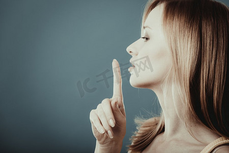 特写镜头妇女要求沉默或秘密与手指在嘴唇安静手势，在蓝色背景