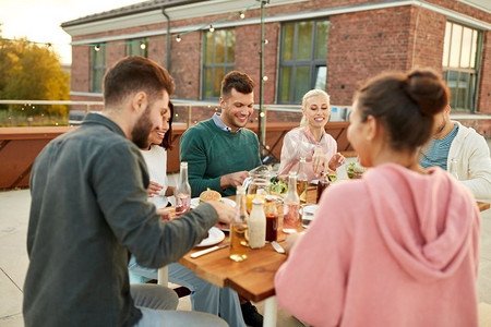 正在吃饭的女人摄影照片_休闲和人的概念-快乐的朋友在夏天在屋顶上的晚宴上吃饭。朋友们在夏天吃晚餐或在屋顶上聚会
