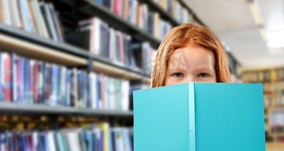 童年与人的概念-微笑的红发女孩在图书馆读书背景。微笑的红发女孩在图书馆看书