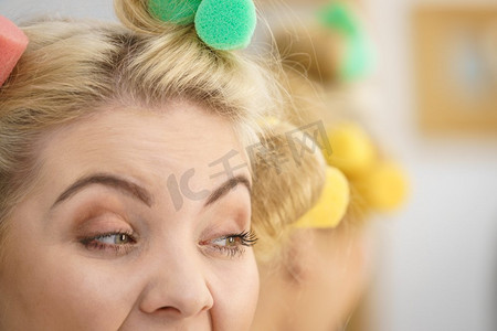 一位金发女子用卷发机在她的发型上创造出漂亮的发型。一名金发女子使用发卷