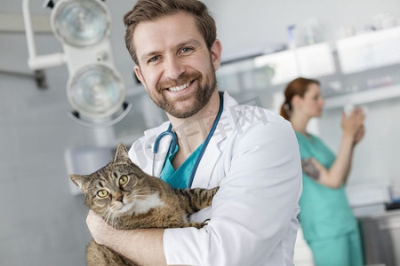 抱猫医生摄影照片_站在兽医诊所微笑的医生抱着猫的肖像