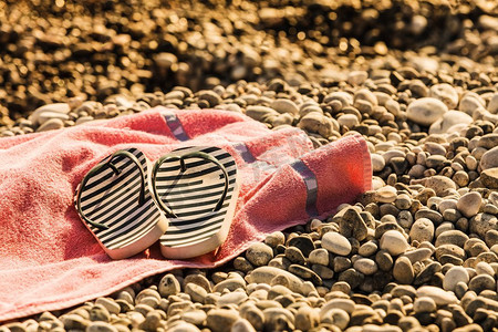 沙滩配件的毛巾日光浴。鞋子凉鞋人字拖，石头石头沙子。日光浴毛巾上的人字拖