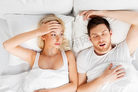 睡眠问题和人们的概念--不快乐的女人和打呼噜的男人躺在床上。不快乐的女人在床上和打呼噜的熟睡的男人