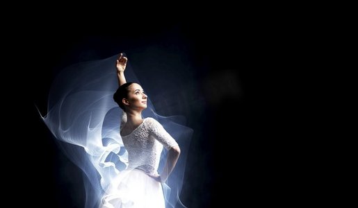 优雅的女舞蹈家在白色礼服反对黑暗背景。跳芭蕾舞演员