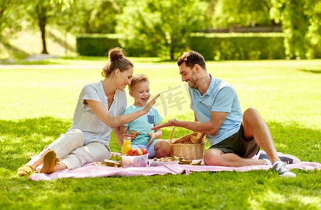 家庭，休闲和人的概念—快乐的母亲，父亲和小儿子在夏季公园野餐。快乐的家庭有野餐在夏天公园