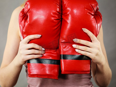 无法辨认的运动女子拿着红色拳击手套。工作室拍摄在灰色背景。女子拿着红色拳击手套