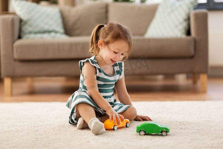 童年和人的概念—快乐的三岁女婴玩玩具车在家里。快乐的女婴玩玩具车在家里