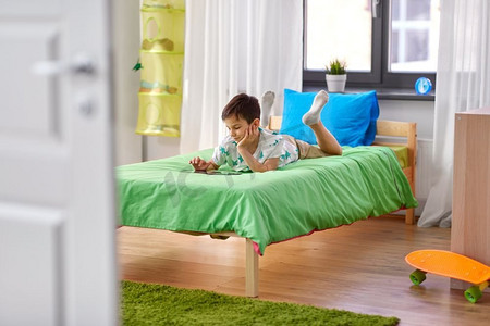 app摄影照片_童年，技术和人的概念—男孩与平板电脑电脑躺在床上在家里。男孩与平板电脑电脑躺在床上在家里