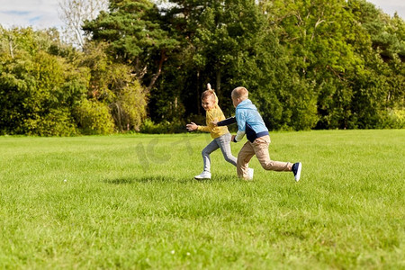 草坪和人摄影照片_童年，休闲和人的概念—两个快乐的男孩玩标签游戏和运行在草坪在公园。两个快乐的男孩玩标签游戏在公园