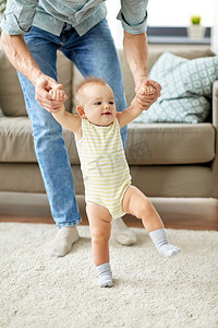 家庭，蹒跚学步和婴儿时代的概念—父亲帮助小宝贝女儿在家里走路。父亲帮助婴儿女儿与步行在家