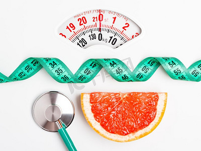 鳞片摄影照片_饮食健康饮食体重控制理念。葡萄柚，白鳞片上有卷尺和听诊器