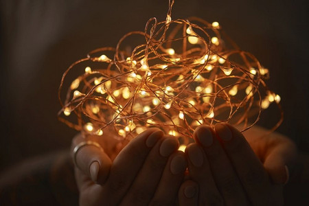 一个女孩的手拿着圣诞灯的花环在黑暗的背景。女人的手在黑暗中握着一串灯。