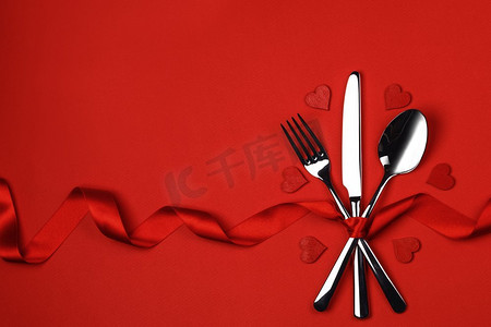 红色的的心摄影照片_餐具套装上系着丝带和心形的红色背景情人节晚餐概念。餐具套装和心形