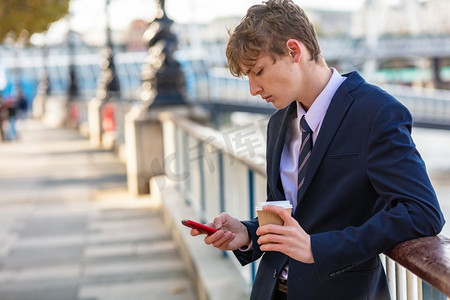 男性年轻成年青少年穿着西装和领带使用智能手机为socail媒体和喝外卖咖啡