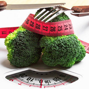 饮食健康饮食体重控制理念。特写绿色西兰花卷尺和白色鳞片上的叉刀