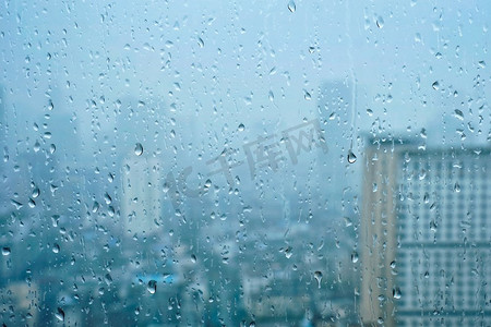 雨水滴在窗口玻璃纹理与摩天大楼在背景。雨点落在窗户上