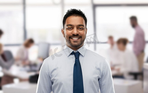 商业和人的概念-微笑的印度商人，穿着衬衫，打着领带，办公室背景。穿衬衫打领带的印度商人在办公室
