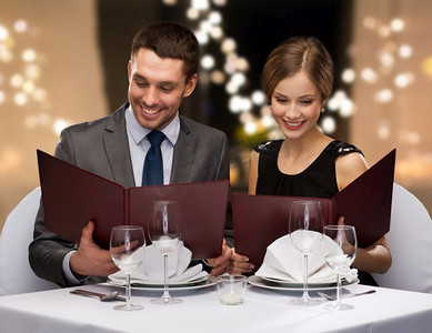 看菜单摄影照片_约会，奢侈品和人的概念—有菜单的愉快的夫妇在餐馆在节日的光在背景一对夫妇在餐厅的菜单
