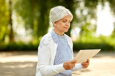 老年、新闻和大众媒体概念—在夏季公园读报的老年妇女。高级妇女阅读报纸在夏季公园