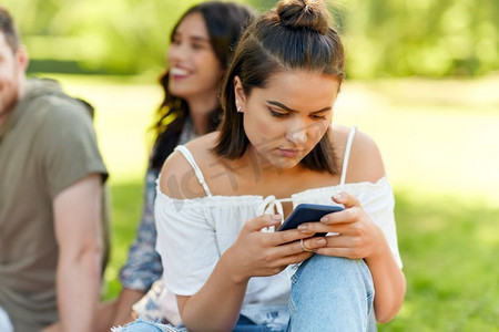 休闲，技术和人的概念—妇女使用智能手机与朋友在夏季公园。妇女使用智能手机与朋友在夏季公园