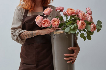 一名有纹身的女子拿着一个大花瓶，上面写着粉红色的媒体玫瑰。母亲节。花店概念。拿着花瓶和一束玫瑰花的女孩