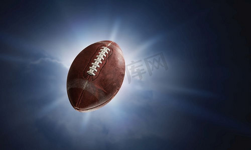 游戏爆炸背景摄影照片_黑暗背景下闪电中的橄榄球。混合媒体。美式橄榄球比赛