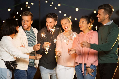 休闲、庆典和人的概念—晚上在屋顶派对上与火花的朋友们欢聚。快乐的朋友与火花在屋顶聚会