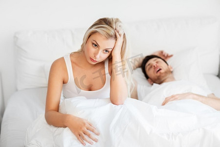 打呼噜摄影照片_睡眠问题和人们的概念--不快乐的女人和打呼噜的男人躺在床上。不快乐的女人在床上和打呼噜的熟睡的男人