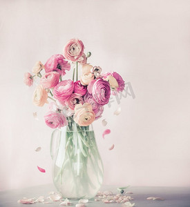 飘落的粉色花瓣摄影照片_餐桌上有玻璃花瓶中飘落的花瓣的粉色毛茅花花束，正视