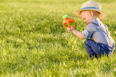 夏天户外摄影照片_户外学步儿童的肖像。一岁男婴戴着草帽用水壶浇水的农村场景