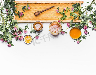 瓶装蜂蜜，带有勺子，蜂窝框架和白色背景下的野花，俯瞰。健康食品，平铺，边框，水平
